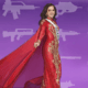 Ilustración estilo caricatura de una reina de belleza mexicana en un vestido de gala rojo con capa, sonriendo contra un fondo morado de acuarela decorado con siluetas blancas de varias armas de fuego.