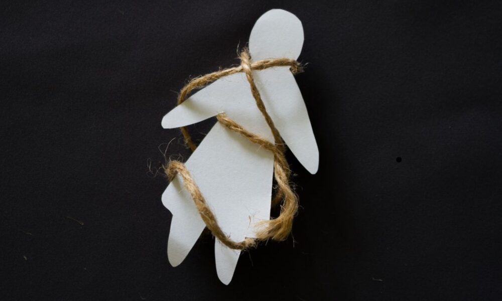 Figuras humanas de papel atadas con cuerda sobre fondo negro, representación simbólica de la trata de personas.