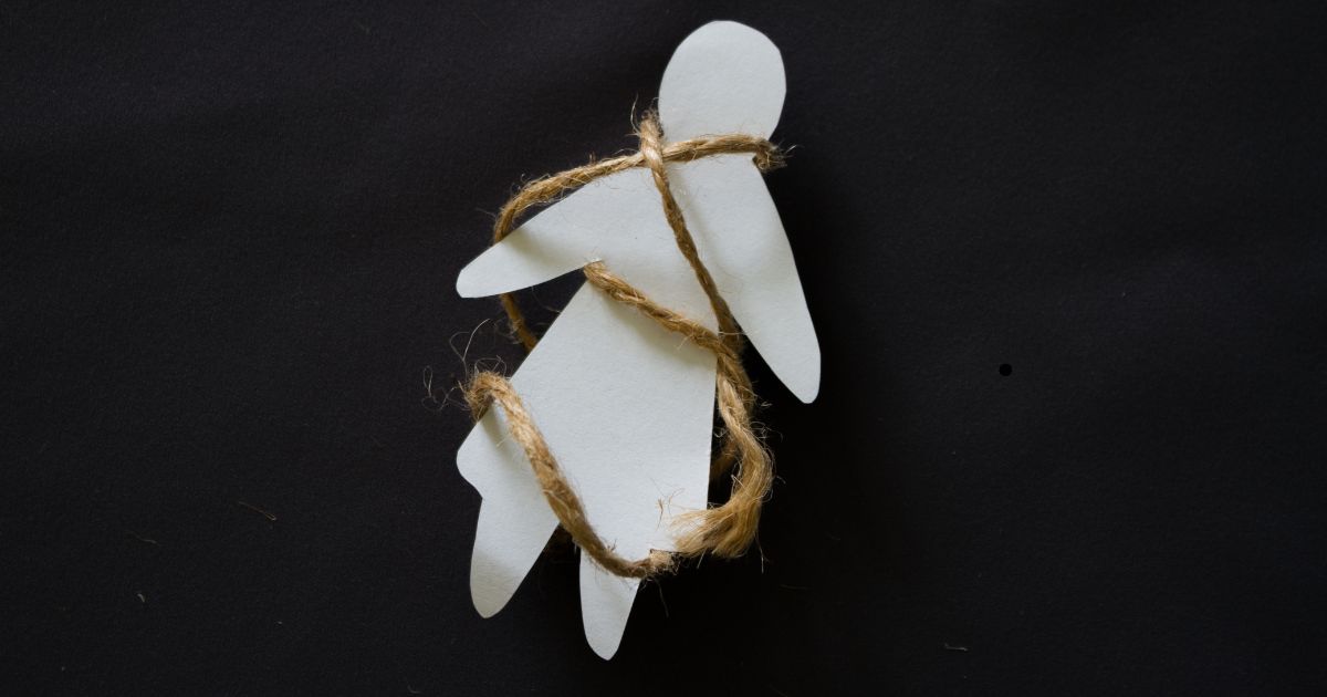 Figuras humanas de papel atadas con cuerda sobre fondo negro, representación simbólica de la trata de personas.